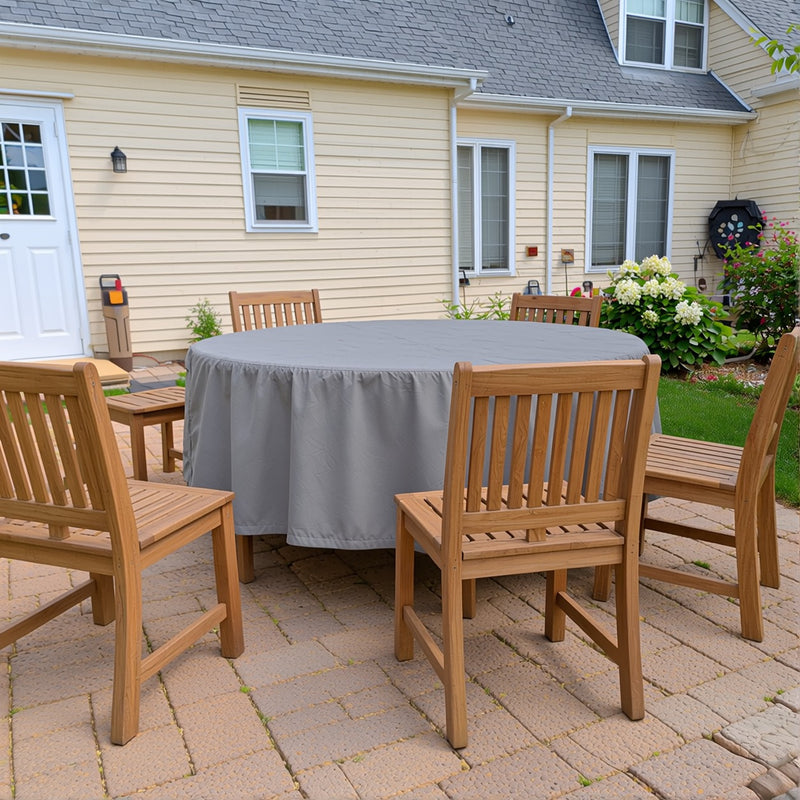 Round patio table covered with a gray Khomo Gear cover in a backyard with wooden chairs